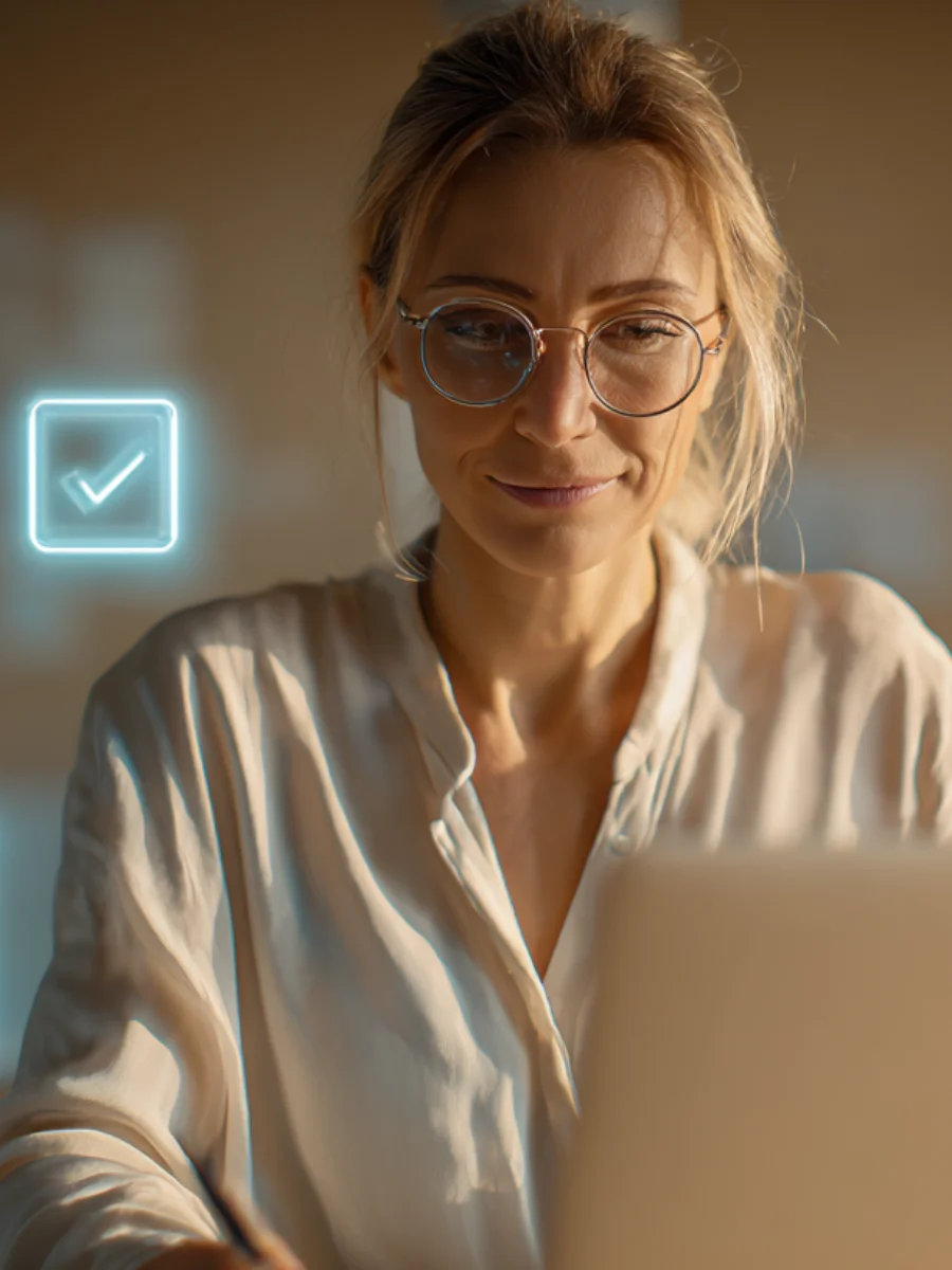 Eine Frau mit Brille arbeitet konzentriert an ihrem Laptop, daneben erscheint ein digitales Häkchen-Symbol – Sinnbild für automatisierte Prozesse, smarte Workflows und effiziente Büroorganisation.